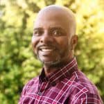 Man in plaid shirt smiling outdoors.